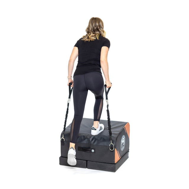 A woman in athletic wear uses the Bells of Steel Soft Glute Bench with attached resistance bands, ideal for hip thrusts and home workouts, shown against a white background.