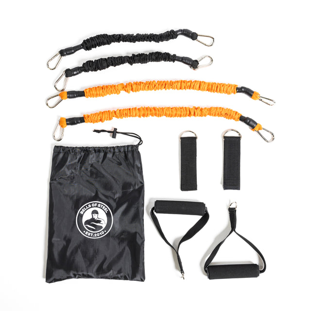 The Bells of Steel Soft Glute Bench set includes two orange and two black resistance bands with carabiner clips, a logo drawstring bag, two handles, and two ankle straps—ideal for home workouts like hip thrusts.