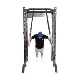 A person in a black T-shirt, gray shorts, and a blue cap is immersed in bodyweight training using Bells of Steel Gymnastics Rings attached to a sturdy metal rack. Positioned in a plank-like stance, they're executing an intensive core workout.