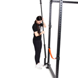 A woman dressed in black workout attire is adjusting a barbell on the Bells of Steel Vertical Mount Barbell Holder Rack Attachment. Set against a white background that highlights both the equipment and her actions, bright orange accents add a vibrant flair to the organization of the home gym.