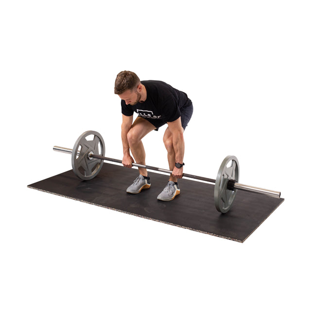 A man in athletic wear bends to grip a barbell while standing on a Bells of Steel Rubber Flooring Gym Mat 39" x 39", ready to lift.