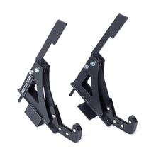 Two black metal Monolift Rack Attachments by Bells of Steel, with angular space-saving designs and bolts, stand upright on a white background. One displays the "BELLS OF STEEL" label.