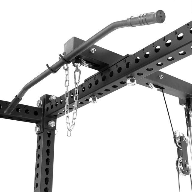 Close-up of a black metal pull-up bar on a power rack with numbered holes, a chain, and the Bells of Steel Lat Pulldown & Low Row Rack Attachment—Hydra & Manticore—mounted nearby for cable exercises.