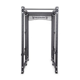 The Manticore Six Post Power Rack Builder by Bells of Steel, featuring modular components, 1" holes for adjustable equipment, and a pull-up bar, displays the brand's logo on the top crossbar. Its sturdy black metal frame is perfect for weightlifting and strength training exercises.