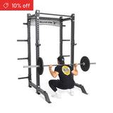 A person in a black shirt and cap performs a barbell squat in the Bells of Steel Manticore Collegiate Power Rack Builder (3" x 3", 1" holes), with weight plates loaded. A "10% off" sale tag appears in the top-left, highlighting this sturdy rack.
