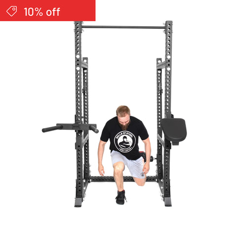A man in a black t-shirt and white shorts kneels inside the Bells of Steel Manticore Half Rack Builder (3" x 3", 1" Holes). A red "10% off" sale banner appears in the top left—ideal for any home gym setup.