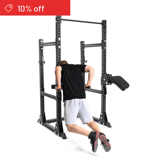 A person in black and gray does dips on the Bells of Steel Manticore Half Rack Builder (3" x 3", 1" Holes). A "10% off" sale banner appears top left on a white background—the perfect home gym upgrade.