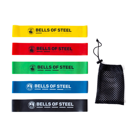 Bells of Steel Mini Bands—five colored resistance bands (yellow, red, green, blue, black) are lined up beside a black mesh drawstring pouch, making them ideal portable workout accessories.
