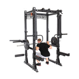 A man in a black shirt and shorts squats confidently with a barbell inside the sturdy Manticore Flat Foot Power Rack by Bells of Steel, which boasts a 1,000-pound capacity and features attachments like weight storage pegs, safety bars, and pull-up handles.