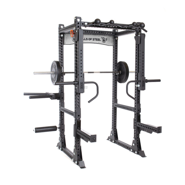 A Bells of Steel Manticore Flat Foot Power Rack in black set up for squats with a barbell and weights. It features pull-up bars, safety bars, modular components with various attachments, and a 1,000-pound capacity, with the brand logo visible on the top crossbar.