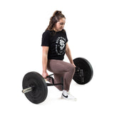 A woman in a black t-shirt, mauve leggings, and white sneakers performs a lunge with the Bells of Steel Open Trap Bar / Hex Bar against a white background.