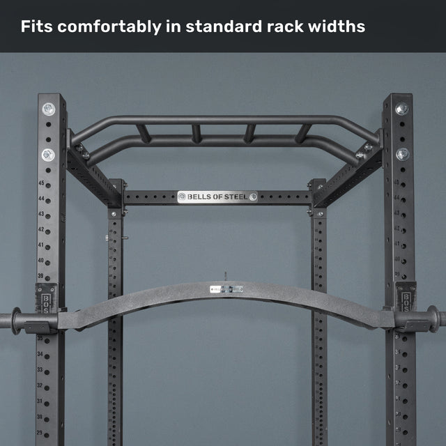 A black pull-up bar is mounted inside a Bells of Steel power rack, with text above stating, "Fits comfortably in standard rack widths." The Arch Nemesis Swiss Bar and cable attachments add versatility.