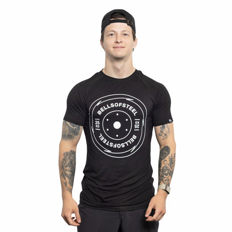 A tattooed person in a black Bells of Steel Bamboo T-Shirt and a backward black cap stands smiling, facing forward against a plain white background.