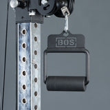 A close-up of the Bells of Steel Fat Bar - Single D Handle cable machine attachment, designed to boost grip strength, is clipped to a metal rack with numbered holes against a gray background.