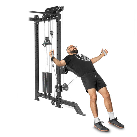 Grinning, a bearded man in a black T-shirt, shorts, white socks, and black sneakers confidently leans back while using the Bells of Steel Aluminum Handles Pair with Bearings on a cable machine. The weight stacks and cables contrast vividly against the white background.