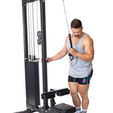 A man in gym wear stands ready to work out, holding the Bells of Steel Tricep Pulldown Rope – Single on a cable machine with one hand while his other hand rests on the equipment, isolated on a white background.