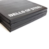 A close-up of the Bells of Steel Trifold Mat, a black non-slip exercise mat with "BELLS OF STEEL" printed in white on the surface.