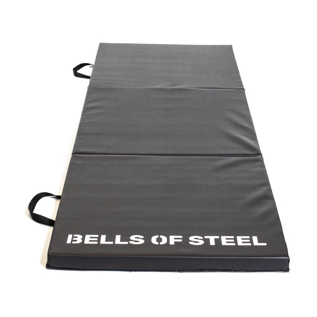 The Bells of Steel Trifold Mat is a black, non-slip exercise mat with side handles and "BELLS OF STEEL" in white text—perfect for gymnastics or workouts.