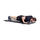 A man wearing a black shirt and shorts performs a push-up on the Bells of Steel Trifold Mat, keeping his body straight, elbows bent, and chest close to the non-slip surface.