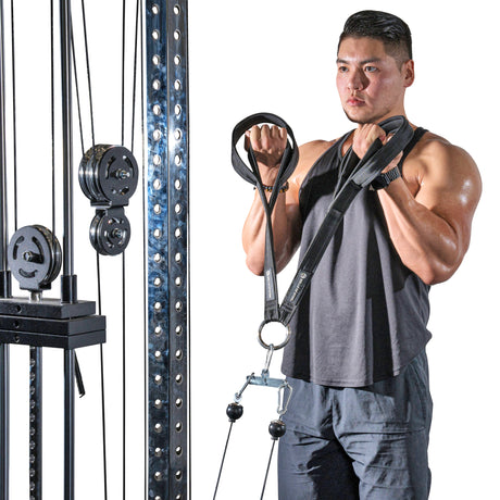 A man in black tank top and shorts uses the Bells of Steel RocIT Tricep Strap attached to a cable machine with visible weights while performing bicep curls.