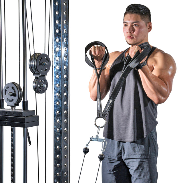 A man in black tank top and shorts uses the Bells of Steel RocIT Tricep Strap attached to a cable machine with visible weights while performing bicep curls.