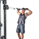 A man in athletic clothing uses the Bells of Steel RocIT Tricep Strap to perform a face pull exercise, pulling the strap attachment toward his face with both hands.