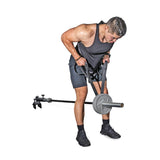 A man in a black tank top and shorts uses the Bells of Steel RocIT Tricep Strap to perform an exercise with a landmine barbell, gripping the bar with both hands while standing on a white background.
