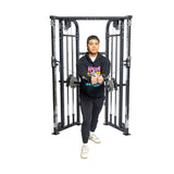 A person intensely uses the Bells of Steel Functional Trainer, pulling cables forward in a staggered stance while wearing black pants, a hoodie, and sneakers, embodying focus and strength through functional training.