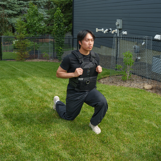 A person wearing the Bells of Steel Weighted Vest and Plates along with black workout clothes performs a lunge on a green lawn in a fenced backyard.