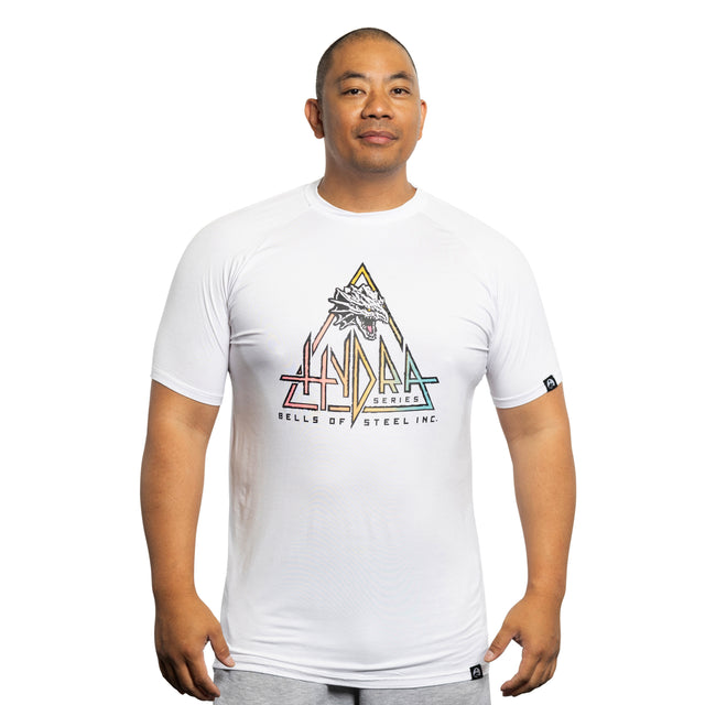 A man wearing a Bells of Steel Bamboo T-Shirt featuring a sweat-wicking fabric, colorful geometric logo, dragon graphic, and the text "HYDRA SERIES" stands against a plain white background.