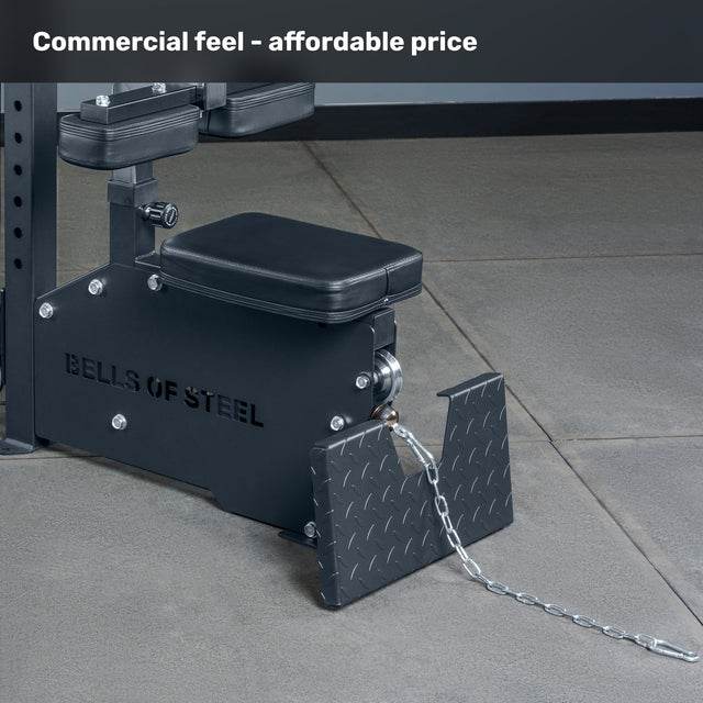 Close-up of a black Bells of Steel Lat Pulldown Low Row Machine with padded seat, footrests, and metal chain on a gray tiled floor. Text above reads, "Commercial feel – affordable price.