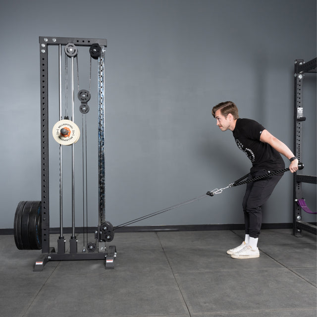 A man in a black t-shirt and pants performs a cable pull-through in the gym using the Bells of Steel Extra Long Tricep Rope Extension (137cm), bent forward with the rope between his legs and attached to a cable machine.